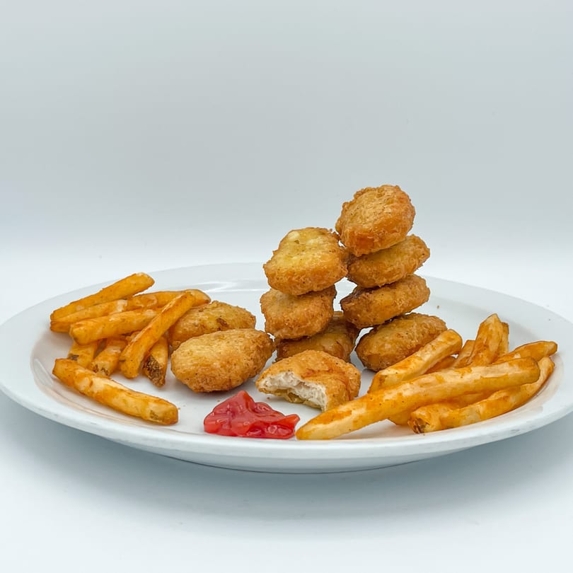 A white plate holds golden-brown Crazy Bob's Cajun Chicken nuggets, fries, and a dollop of ketchup.