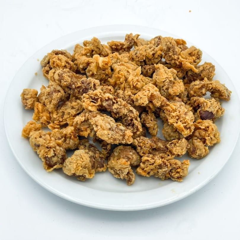 A white plate piled high with golden-brown, crispy fried chicken gizzards from Crazy Bob's Cajun Chicken.