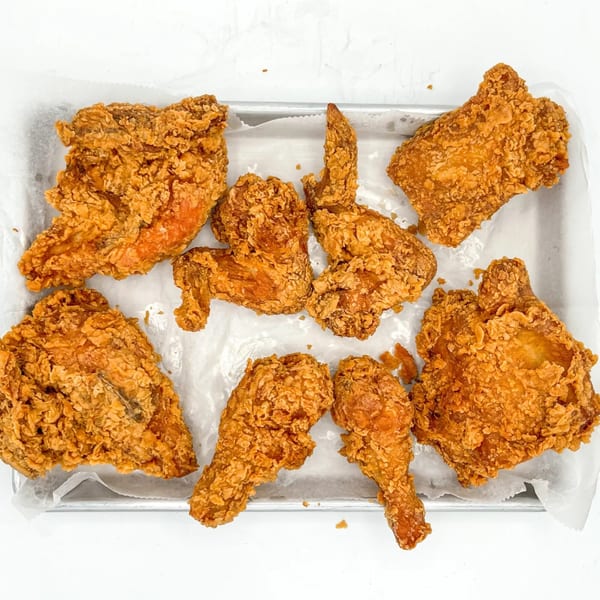 A metal tray filled with various pieces of golden-brown, crispy fried chicken on white parchment paper.