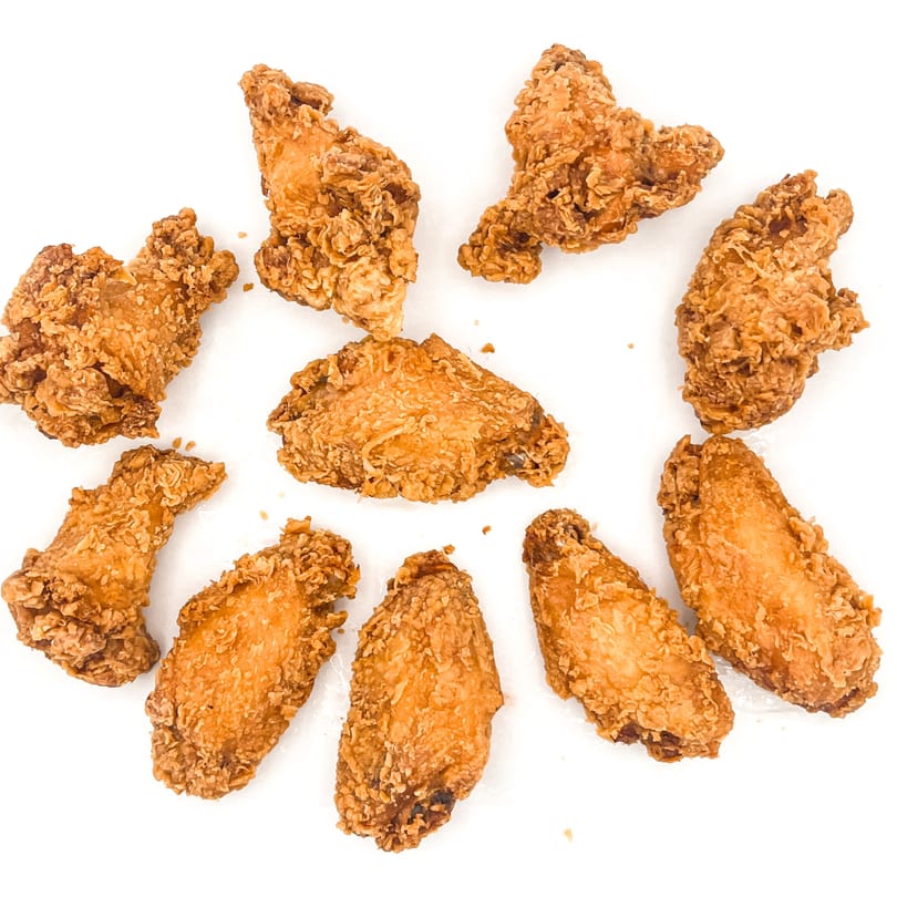 A top-down view of ten crispy, golden-brown fried chicken wings scattered on a white surface.